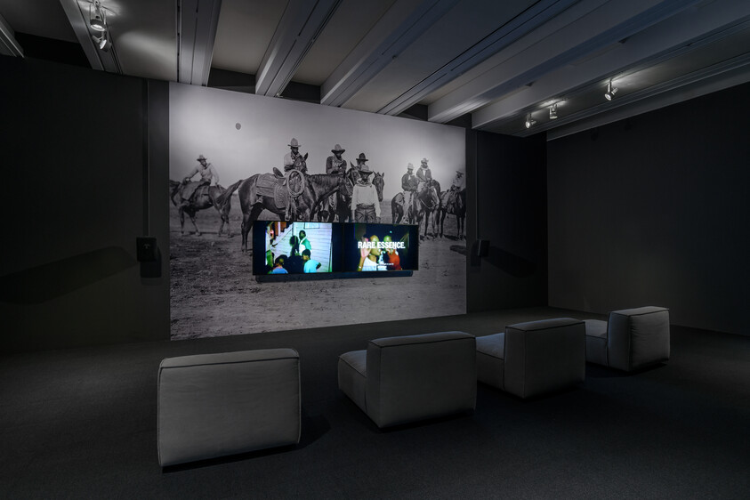 Three padded benches face wall-mounted video screens beneath a large black-and-white mural of cowboys.