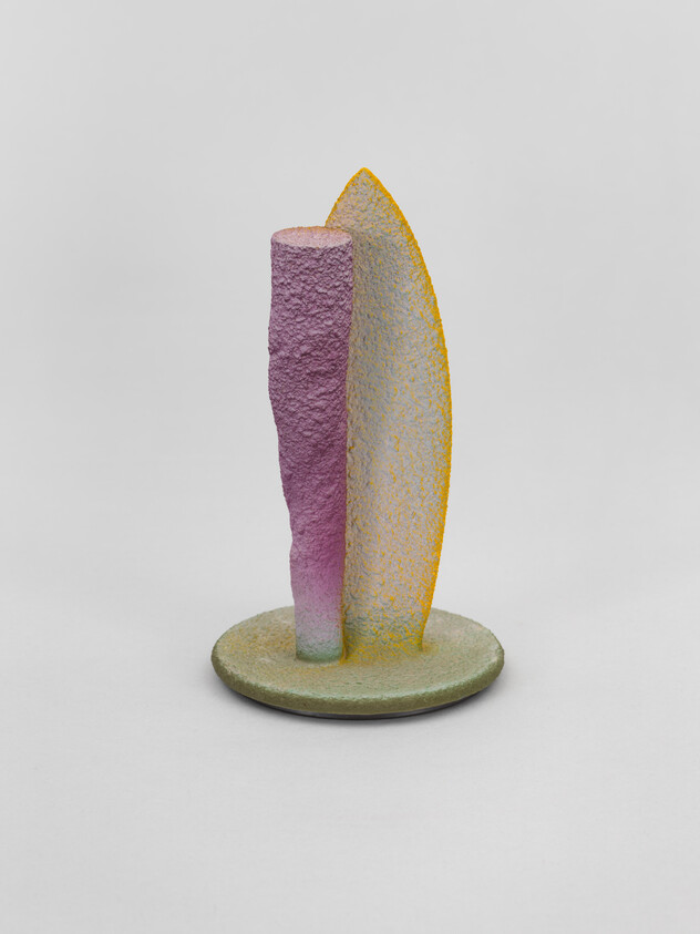A small textured pastel sculpture with a purple column and yellow-edged curved panel on a round base.