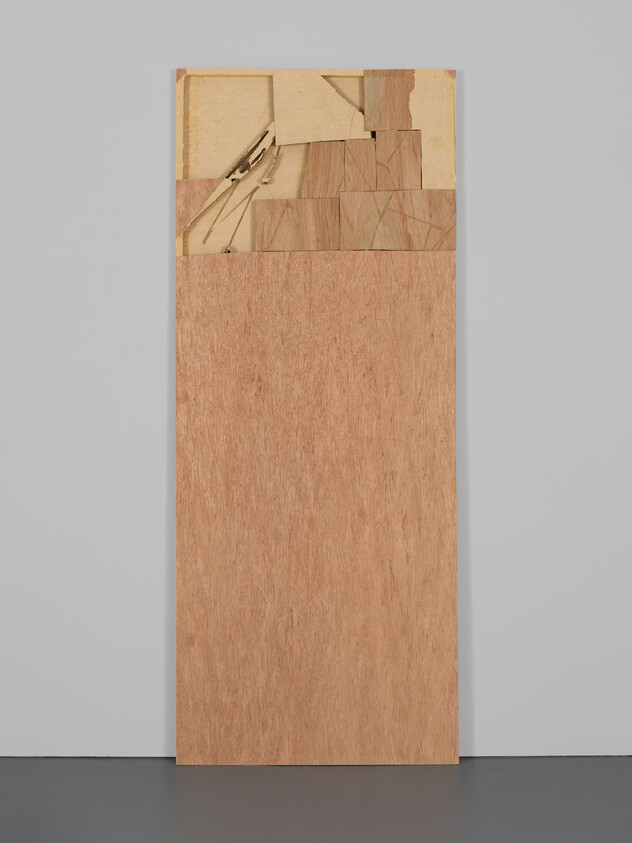 Tall plywood panel leaning against a wall with a patchwork of wood pieces and drafting compass at top.
