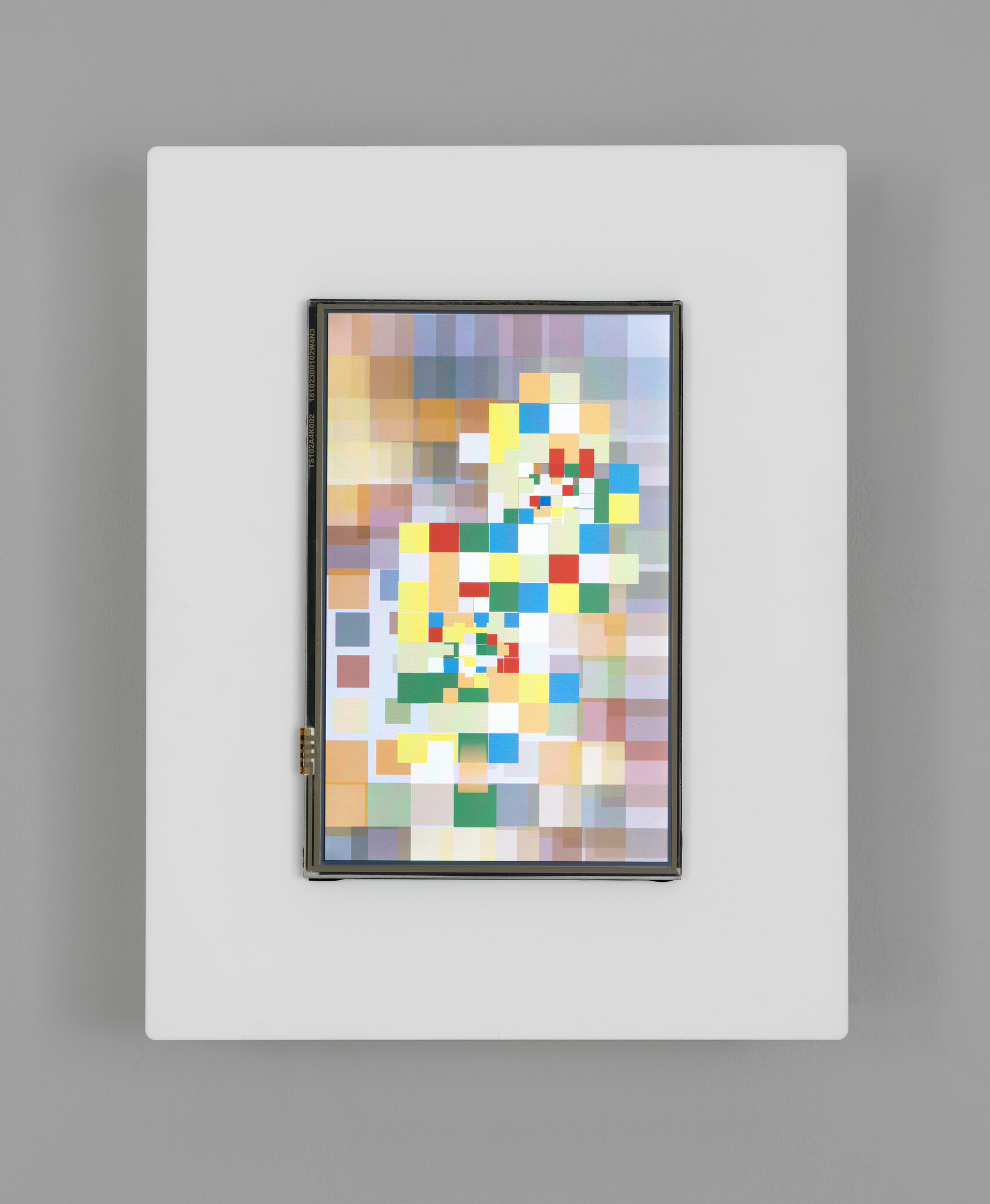 A digital display with a pixelated, colorful abstract image, framed in white, mounted on a gray wall.