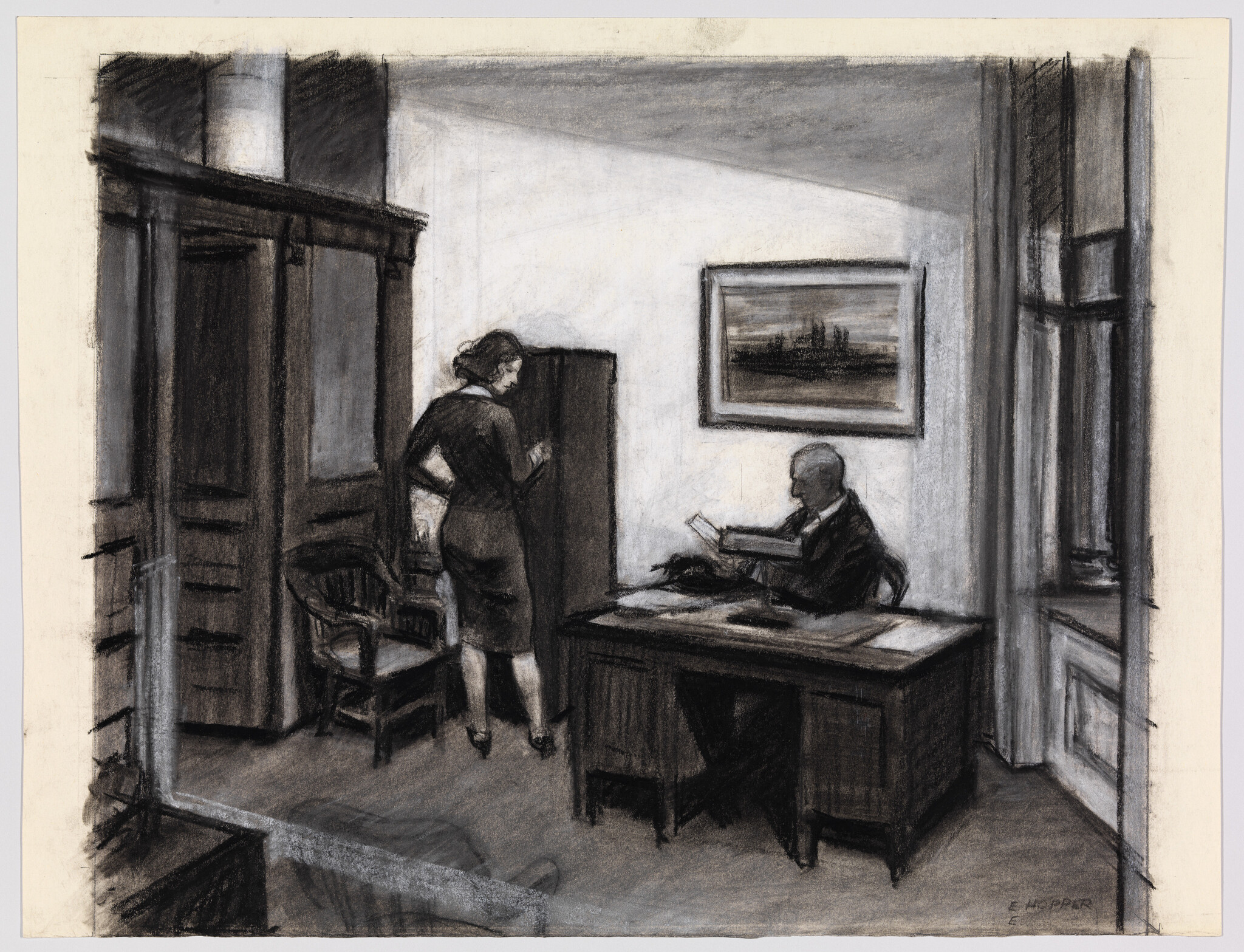 A man reads documents at his desk while a woman stands by a cabinet in the office.