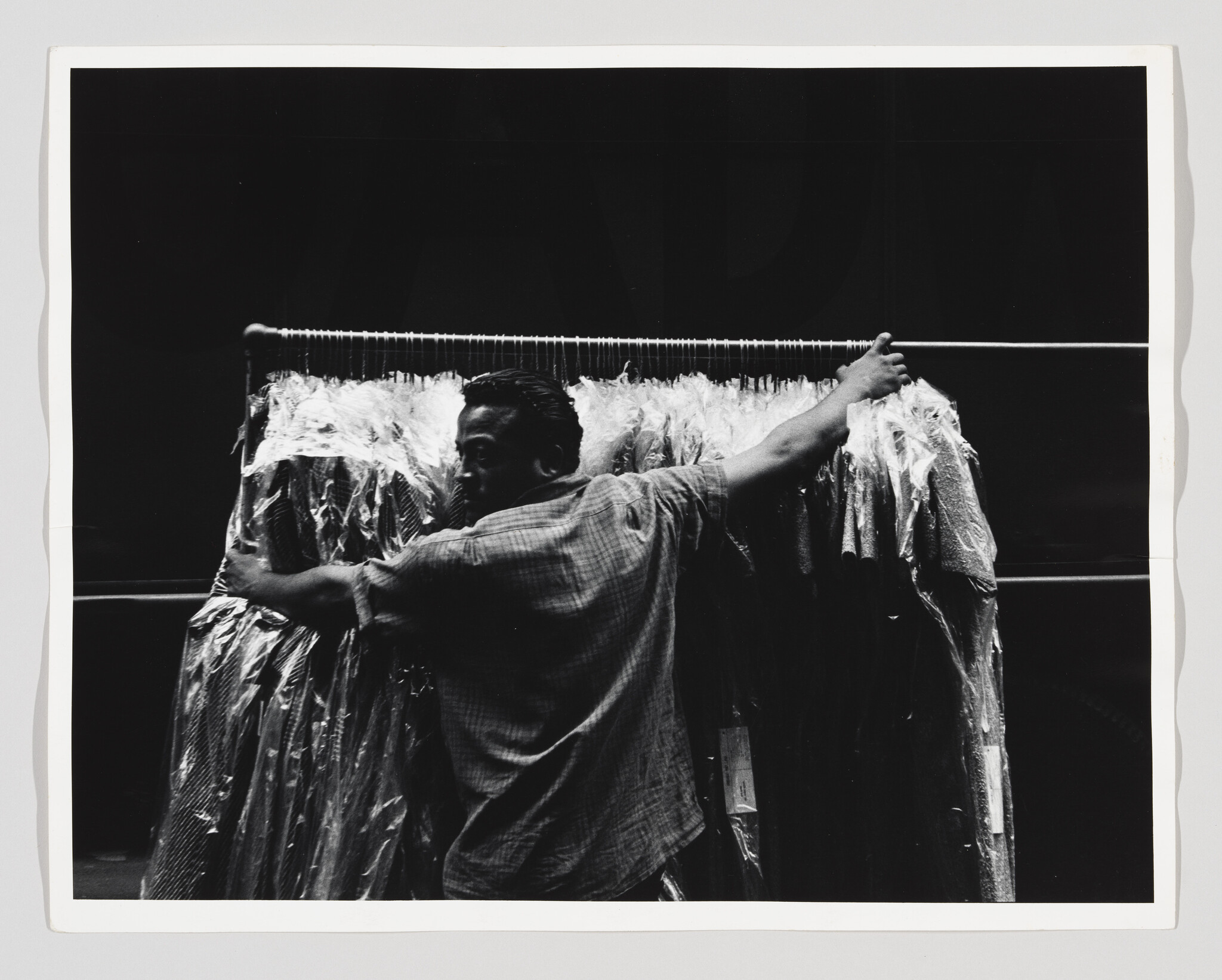 Person carrying a rack of clothes covered in plastic, moving through a dimly lit area.