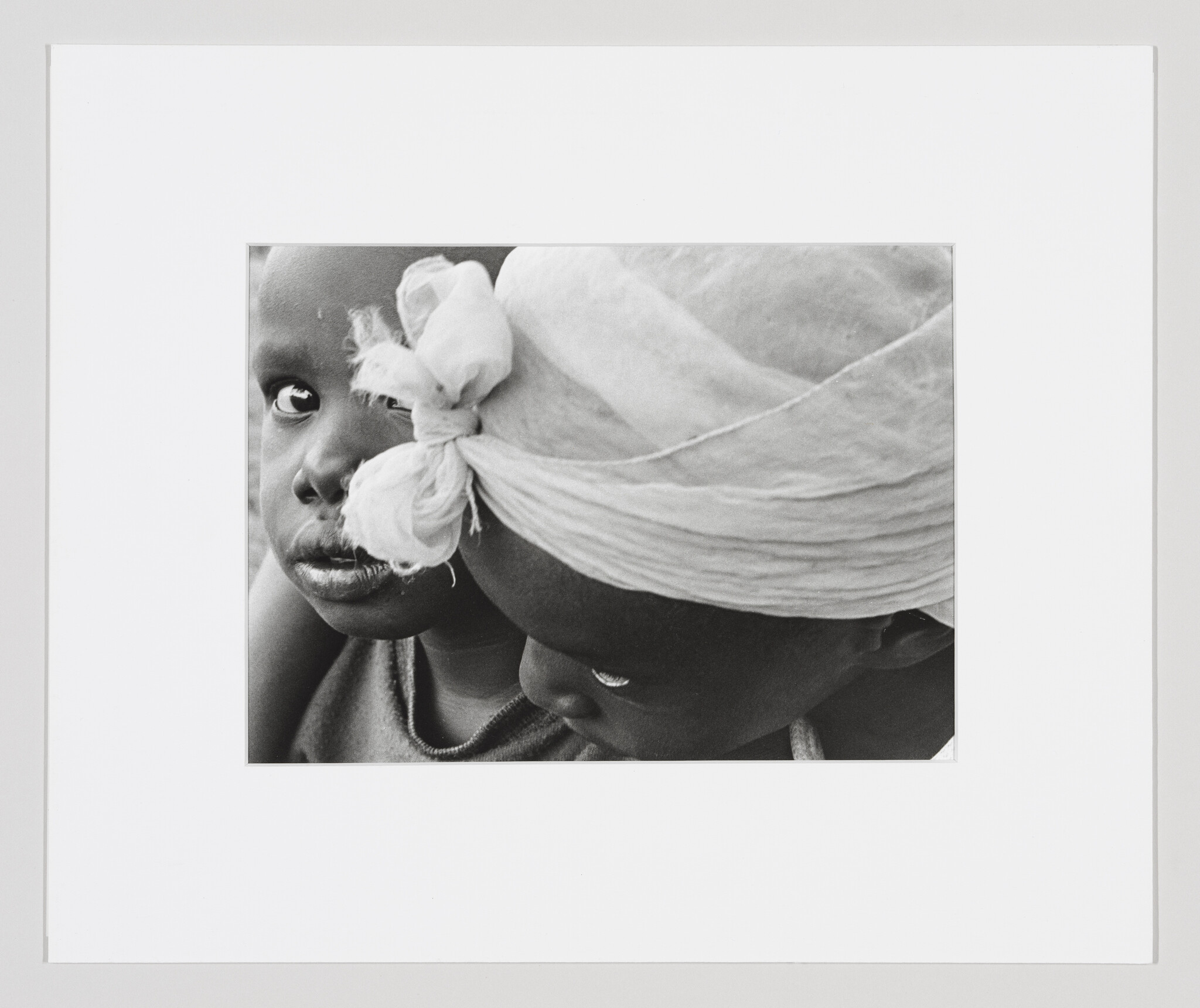 Two children in close embrace, one with a tied headscarf and the other looking directly at the camera.