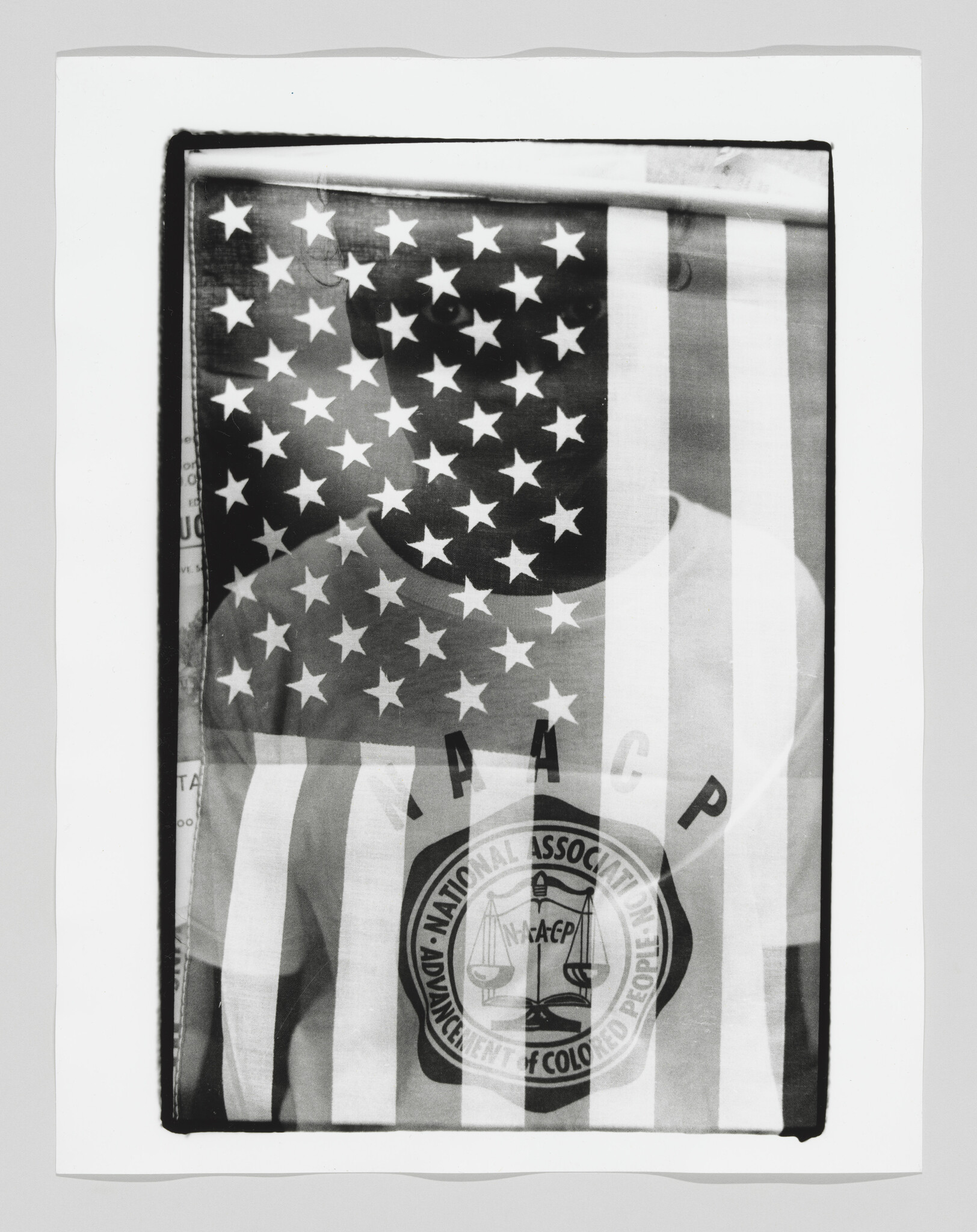 A person stands behind a translucent American flag while wearing an NAACP shirt.