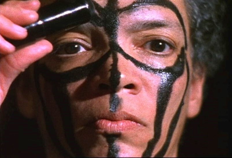Person applying black face paint, creating bold vertical and circular patterns across their face.