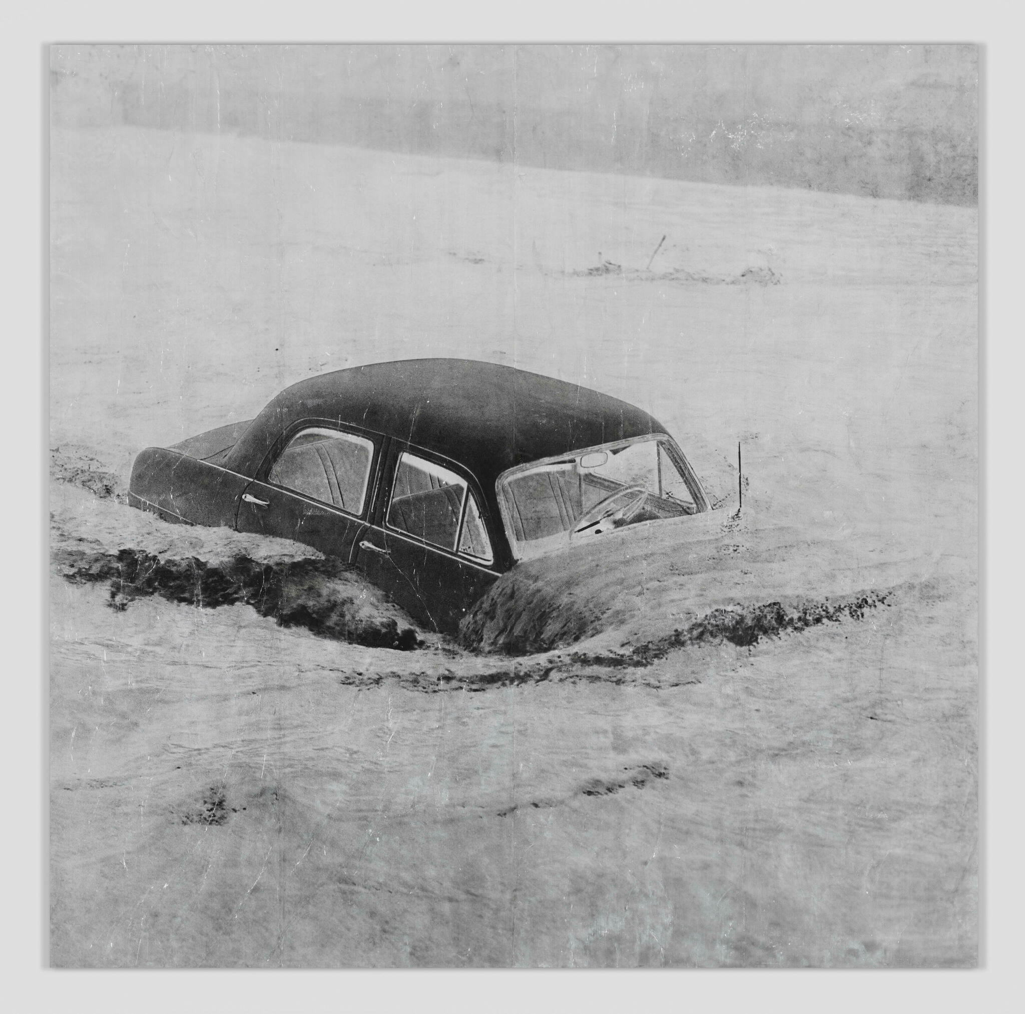 A black and white photo of a car being overtaken by flood waters.