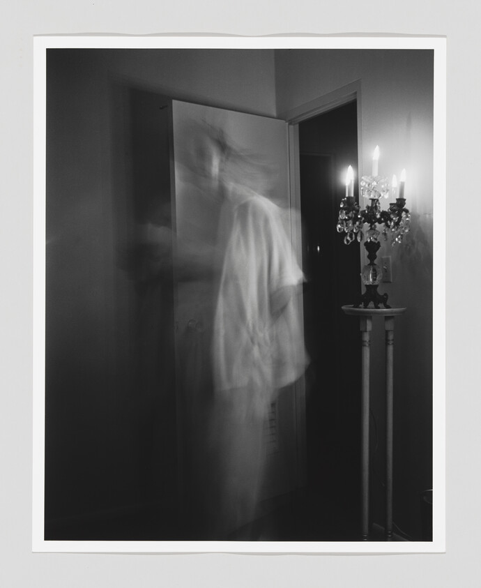A blurred, ghostlike figure moves through a doorway beside a lit candelabrum.