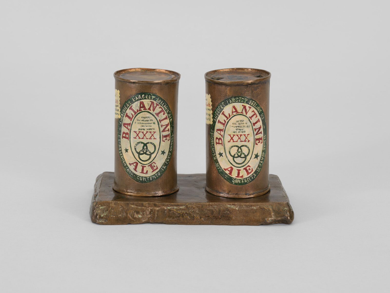 Two bronze Ballantine Ale cans with XXX labels sit side by side on a rectangular base.