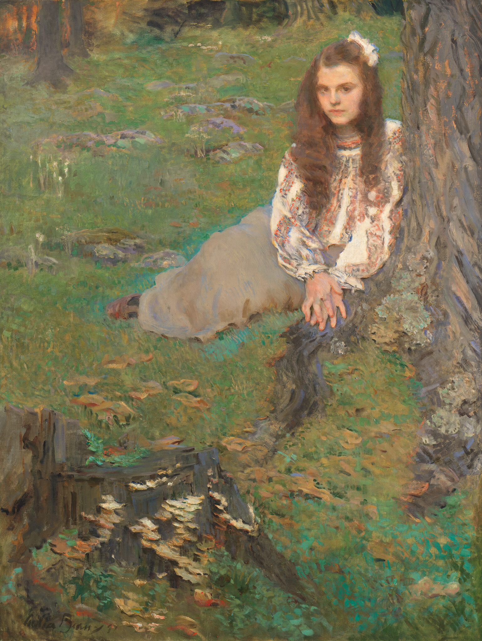 Young woman in embroidered blouse sits against a tree in a green forest clearing.