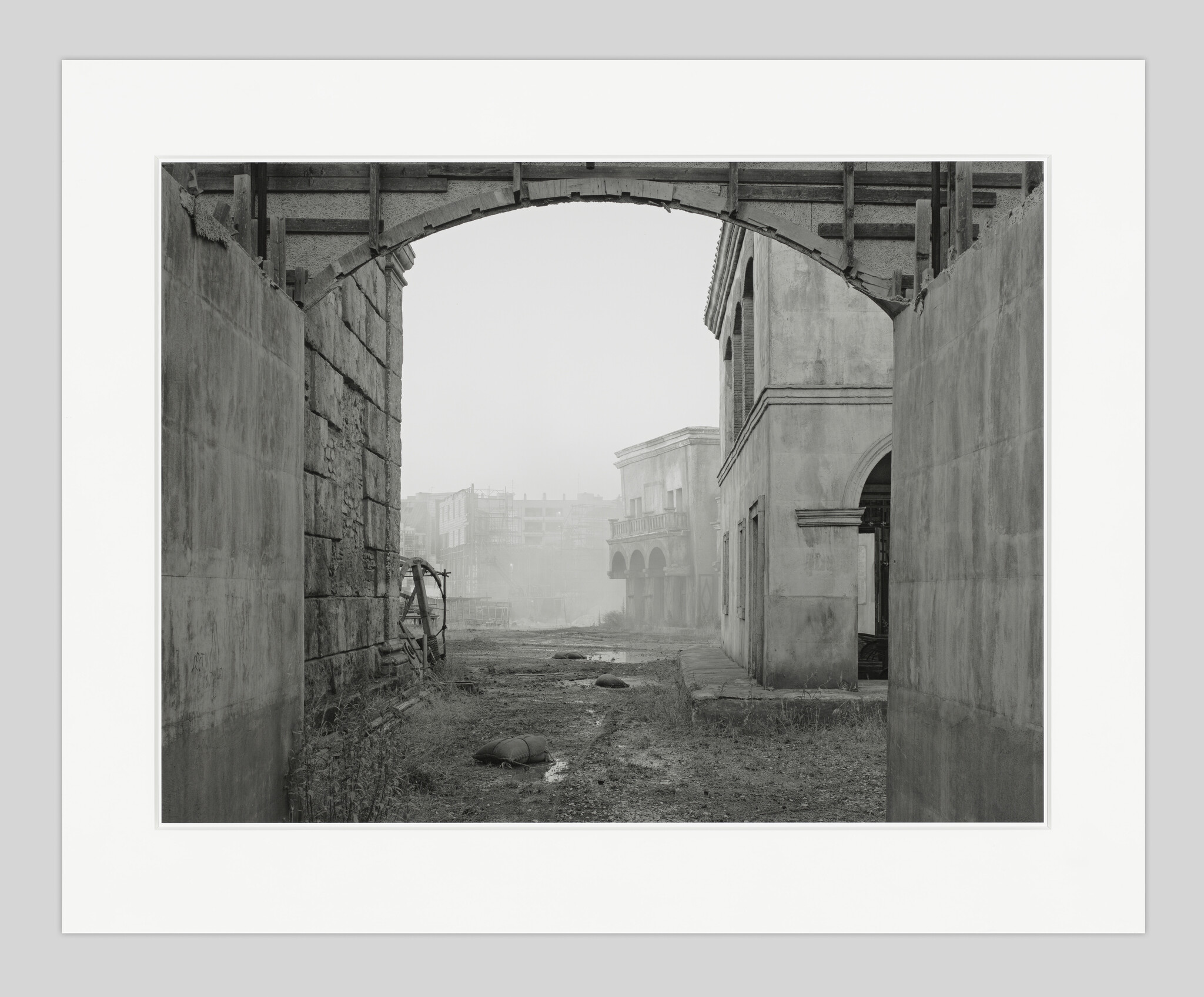 Archway frames a foggy, abandoned street with old buildings and scattered sandbags.