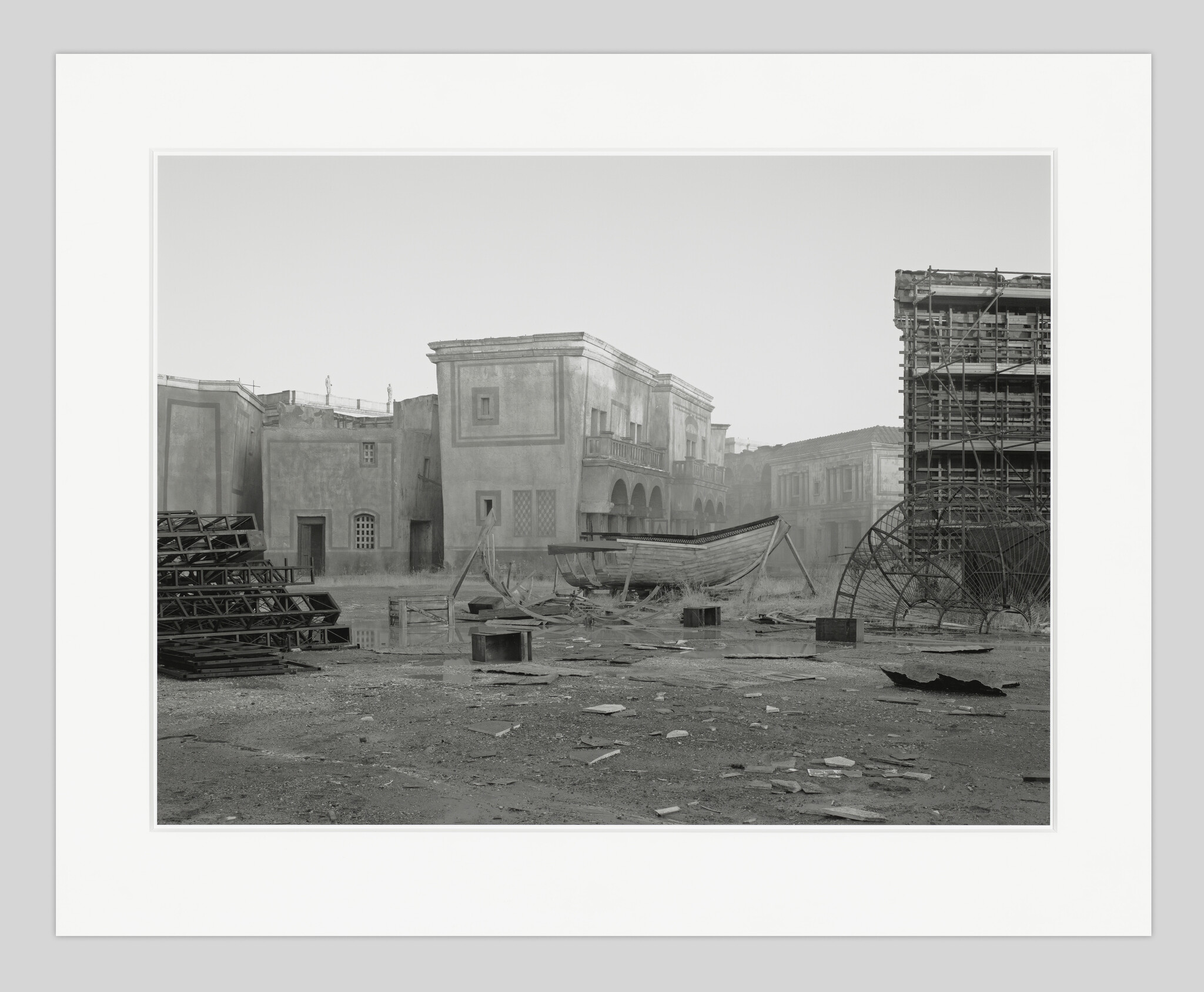 A weathered wooden boat sits on dry ground amid debris and scaffolding.