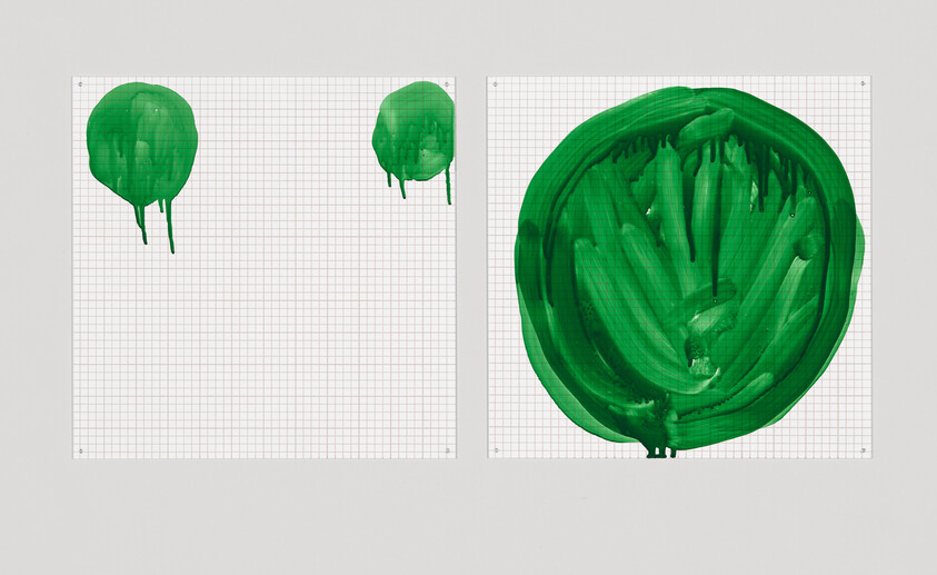 Two pieces of grid paper pinned to a wall, each with a different sized and styled green paint blot. The left sheet has two smaller, more defined blots, while the right sheet features a large, smeared blot dominating the space.
