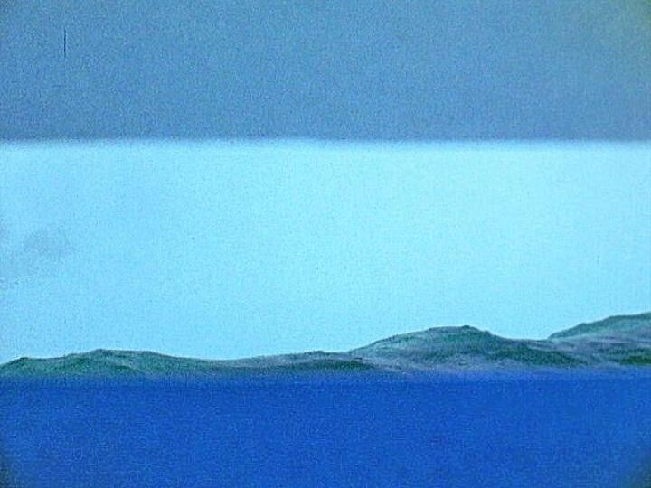 Calm blue sea with low green islands on the horizon under a layered cloudy sky.