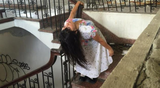 Woman in a floral dress leaning back on a staircase railing.