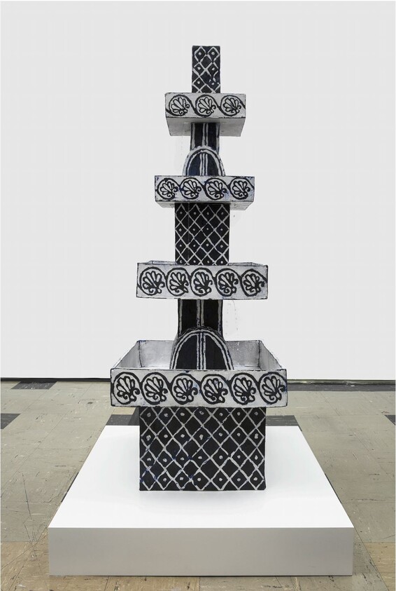 A black-and-white tiered sculptural fountain with geometric and floral patterns displayed on a white plinth.