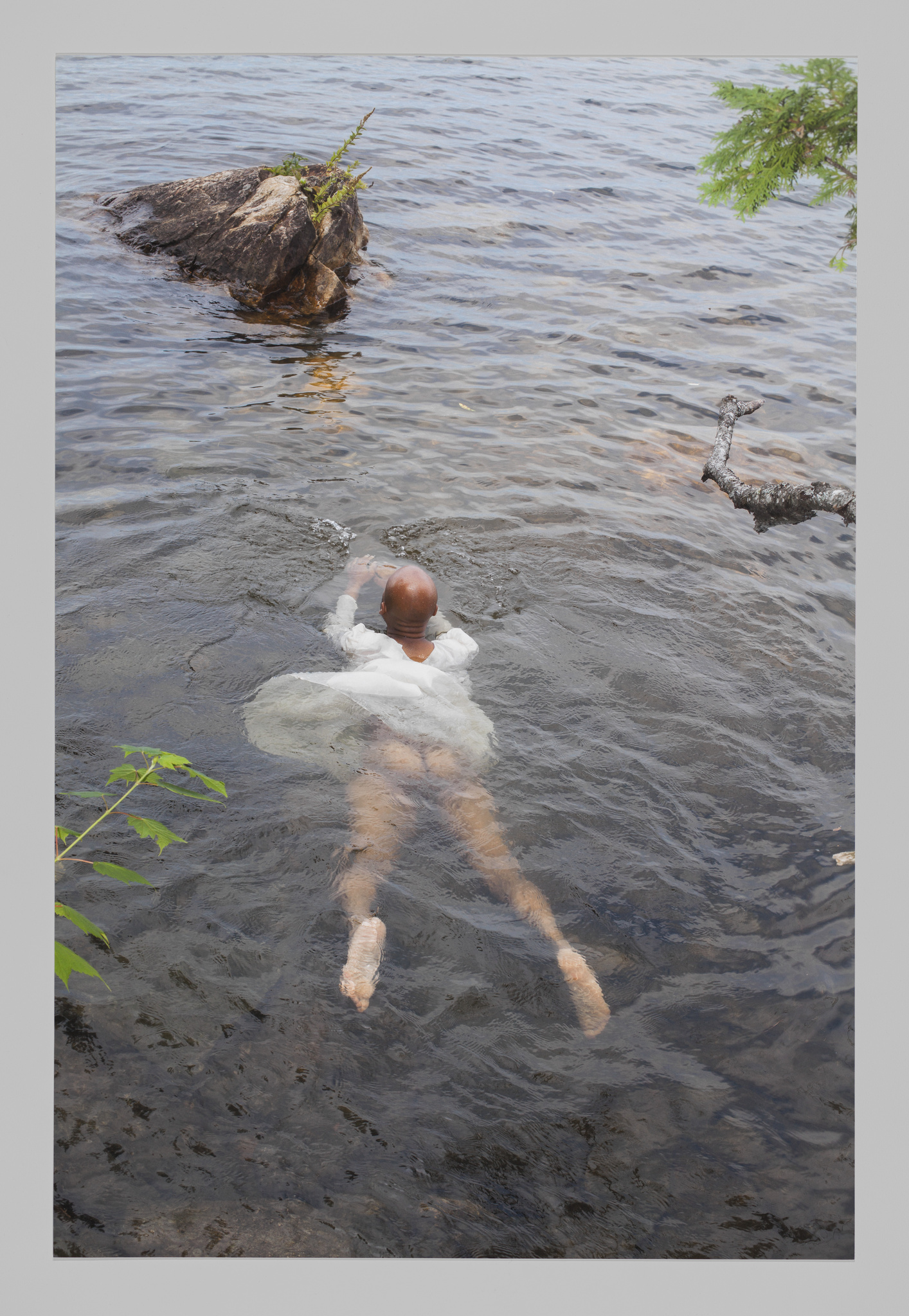 A figure swims out into rippling water, with their dress floating up to reveal their bare bottom and legs