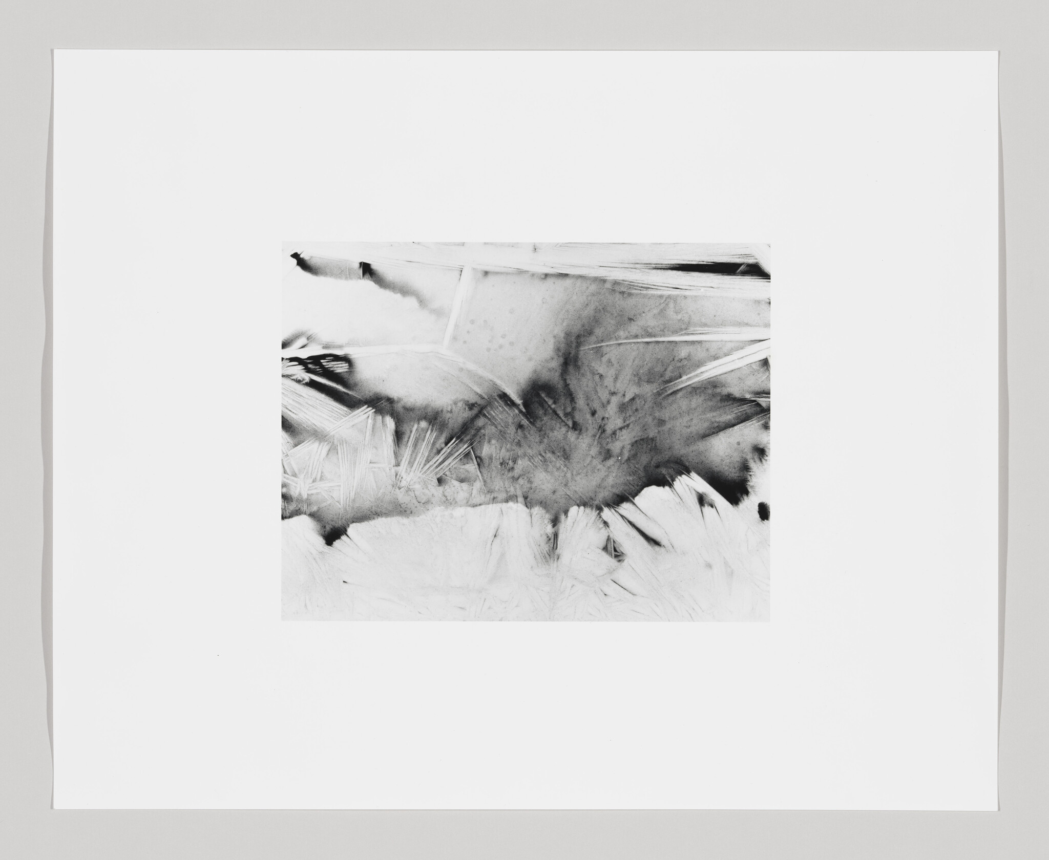 A monochromatic abstract artwork featuring various shades of black, white, and gray, with dynamic strokes and splatters that suggest movement. The piece is mounted on a white background with a wide border, emphasizing its contrast and composition.