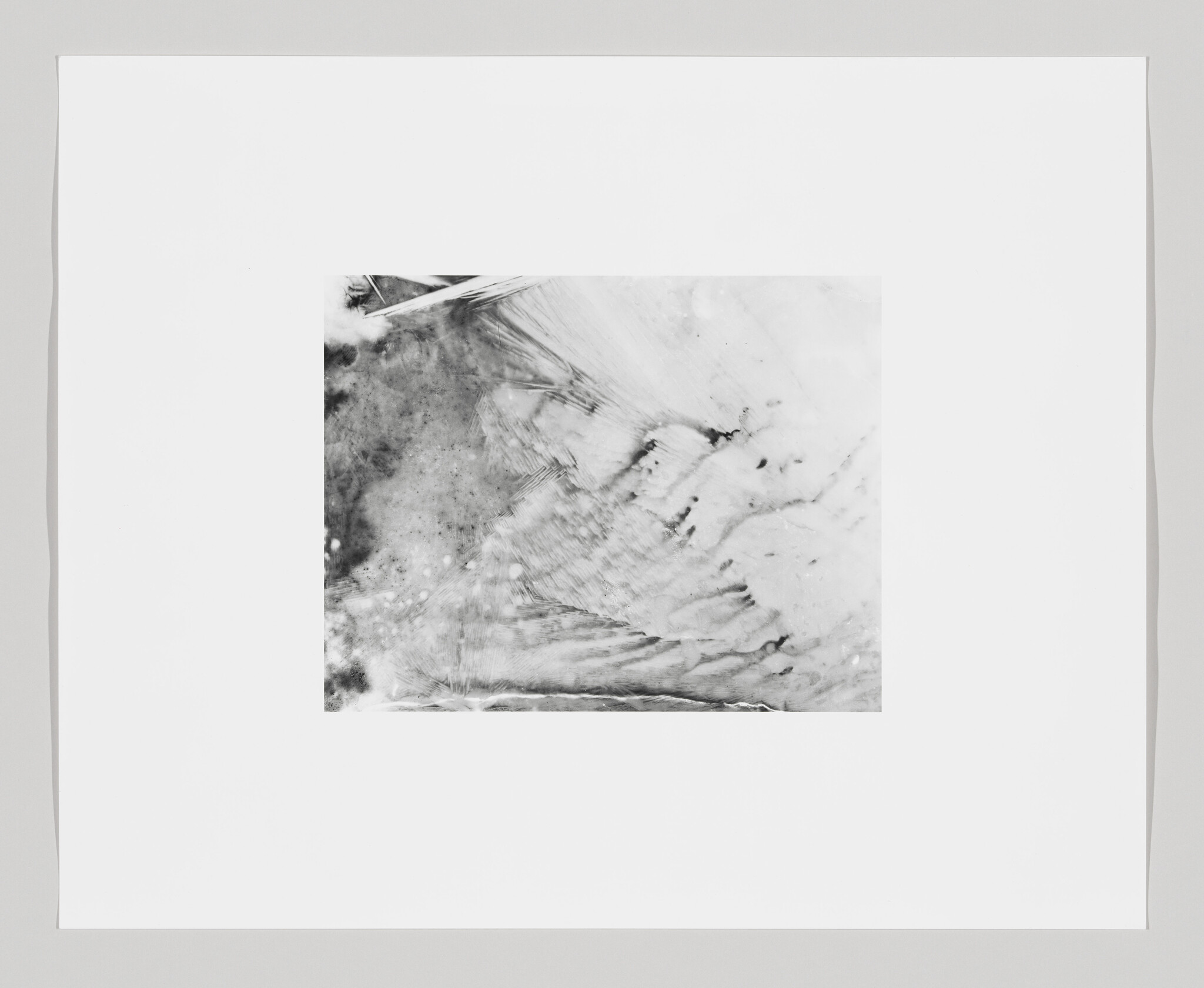 A monochromatic abstract image with textured patterns resembling ice or mineral formations, framed with a wide white border.