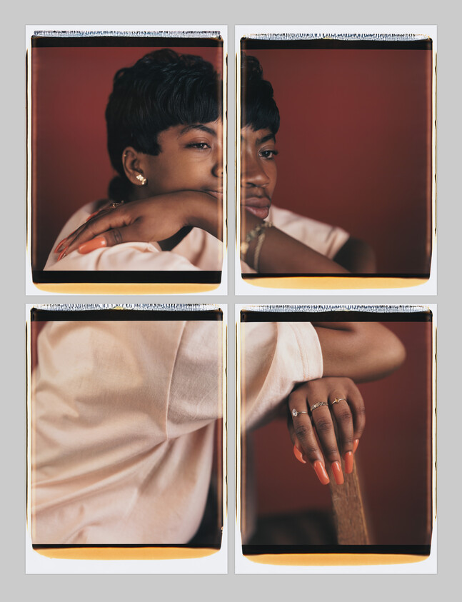 Woman with short hair rests her arms and shows orange-painted nails and rings.