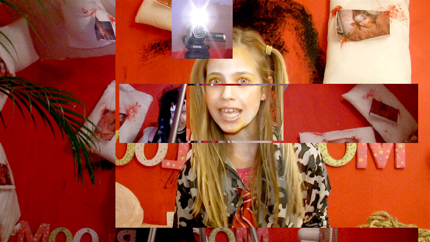 Girl with pigtails speaking to a camera in a red room with collage-like photo strips on the wall.