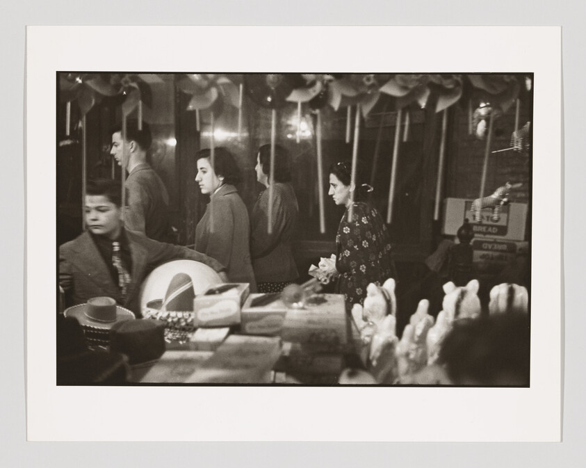 Several shoppers walk past a store display filled with hats, boxes, and ceramic bunnies.