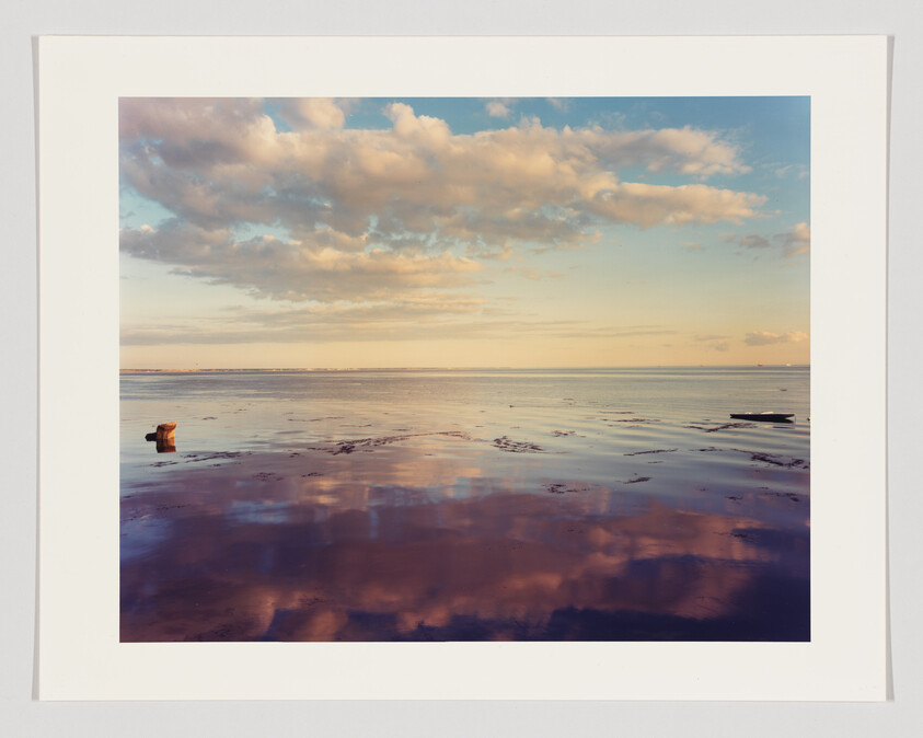A serene seascape with a colorful sky reflected in the calm water at sunset, featuring a single wooden post protruding from the water's surface.