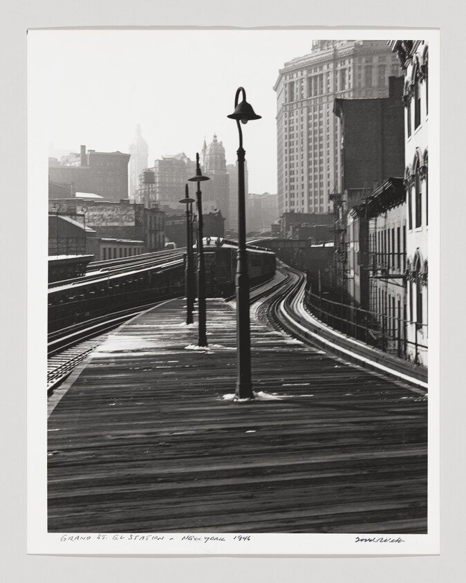 Elevated wooden train platform and curving tracks with lampposts leading into a city skyline.