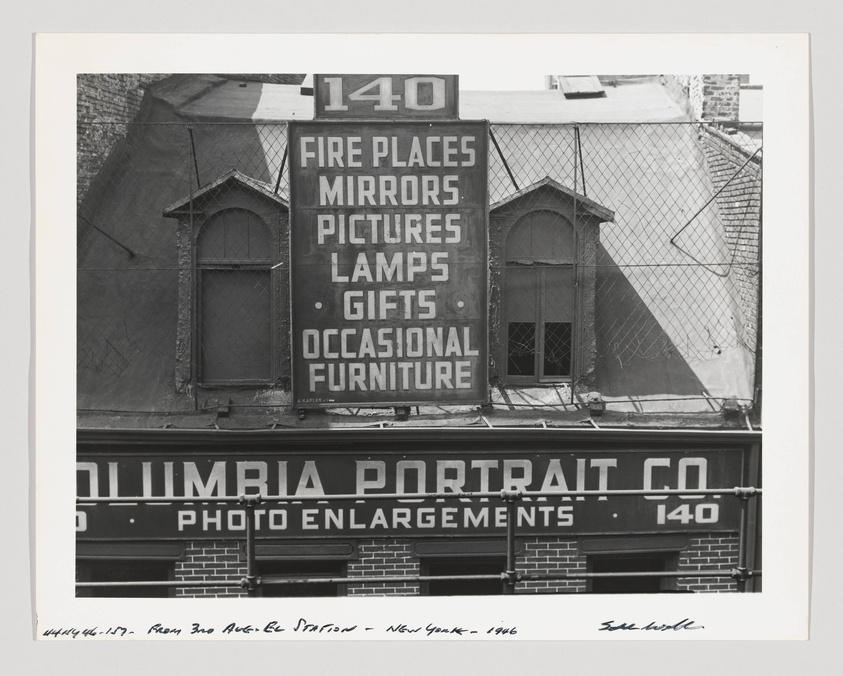 Black and white photograph of the exterior of the Columbia Portrait Co. building at 140, featuring signage for fireplaces, mirrors, pictures, lamps, gifts, and occasional furniture. The photo includes a view of the building's windows and a partial view of the adjacent building, taken from an elevated perspective. Handwritten text at the bottom left indicates the photo was taken from 3rd Ave El Station in New York, 1946, and is signed by the photographer.