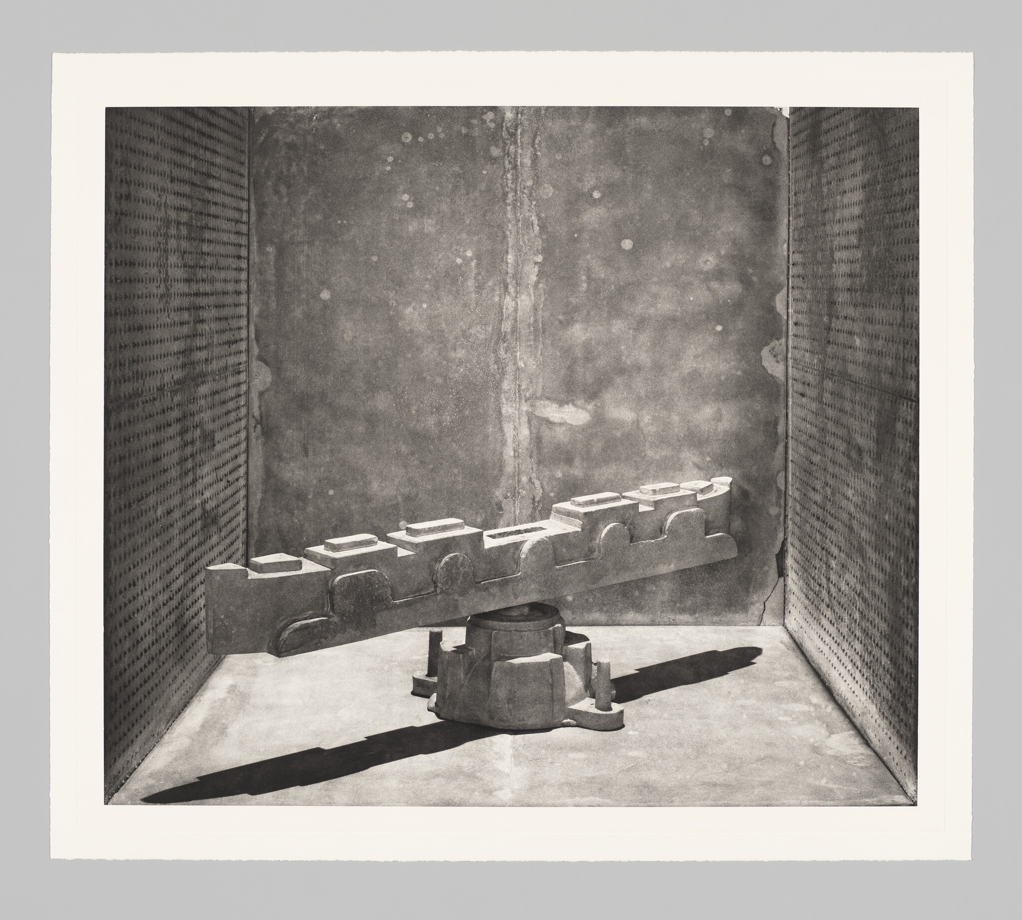 A concrete industrial sculpture resembling a toothed beam rests on a pedestal casting a long shadow.