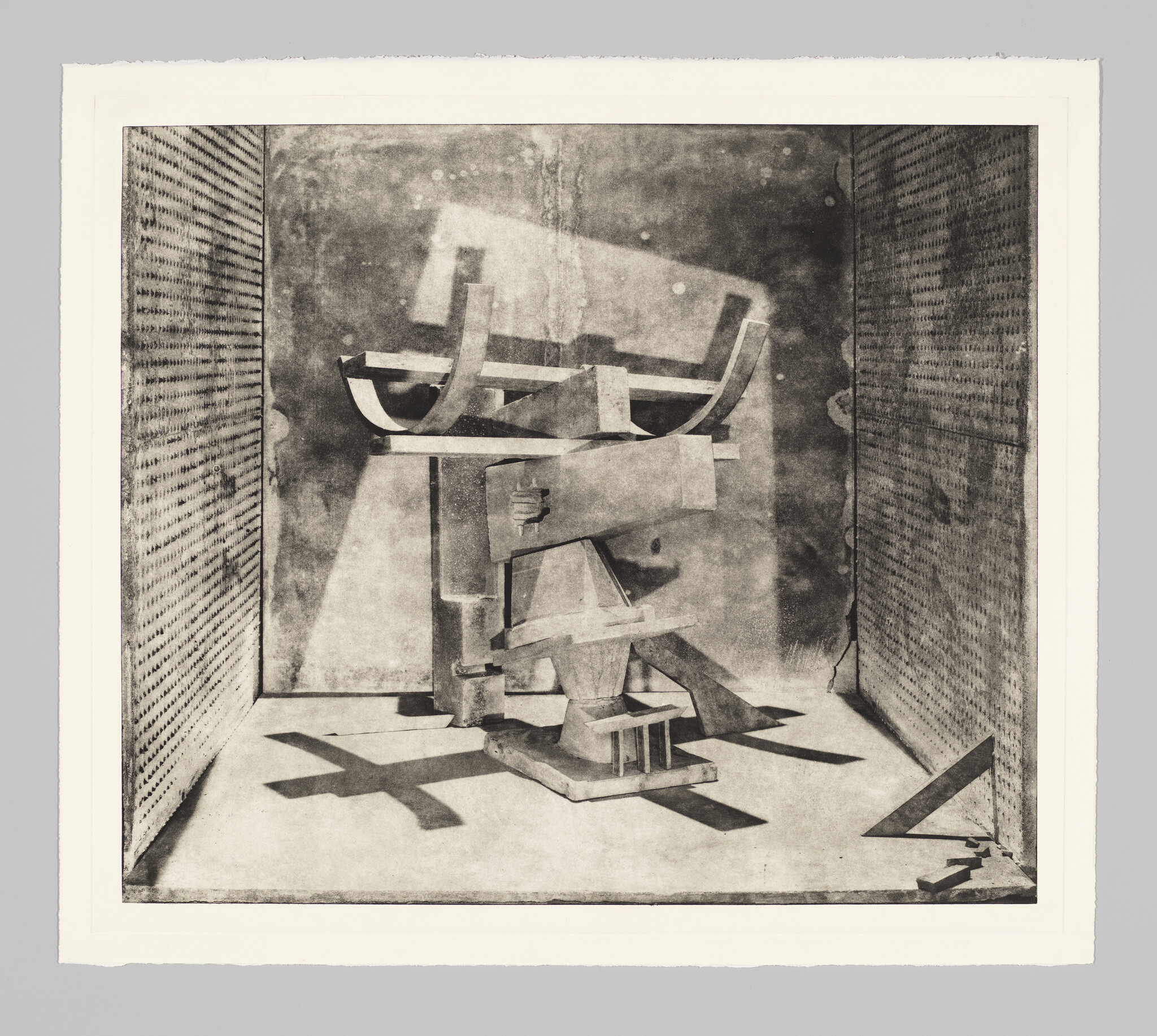 Abstract wooden sculpture made of assembled geometric shapes rests inside a small shadowed display room.