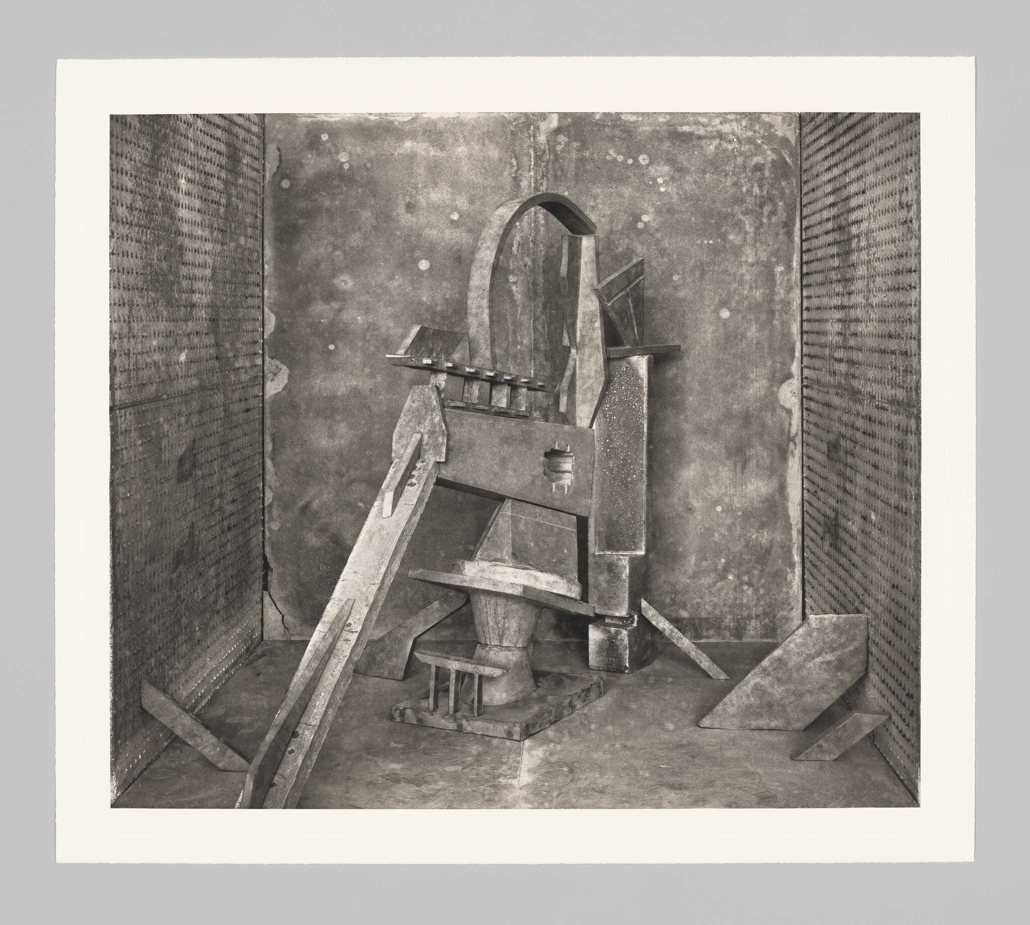 A weathered abstract sculpture made of wooden and metal shapes stands in a small enclosed room.