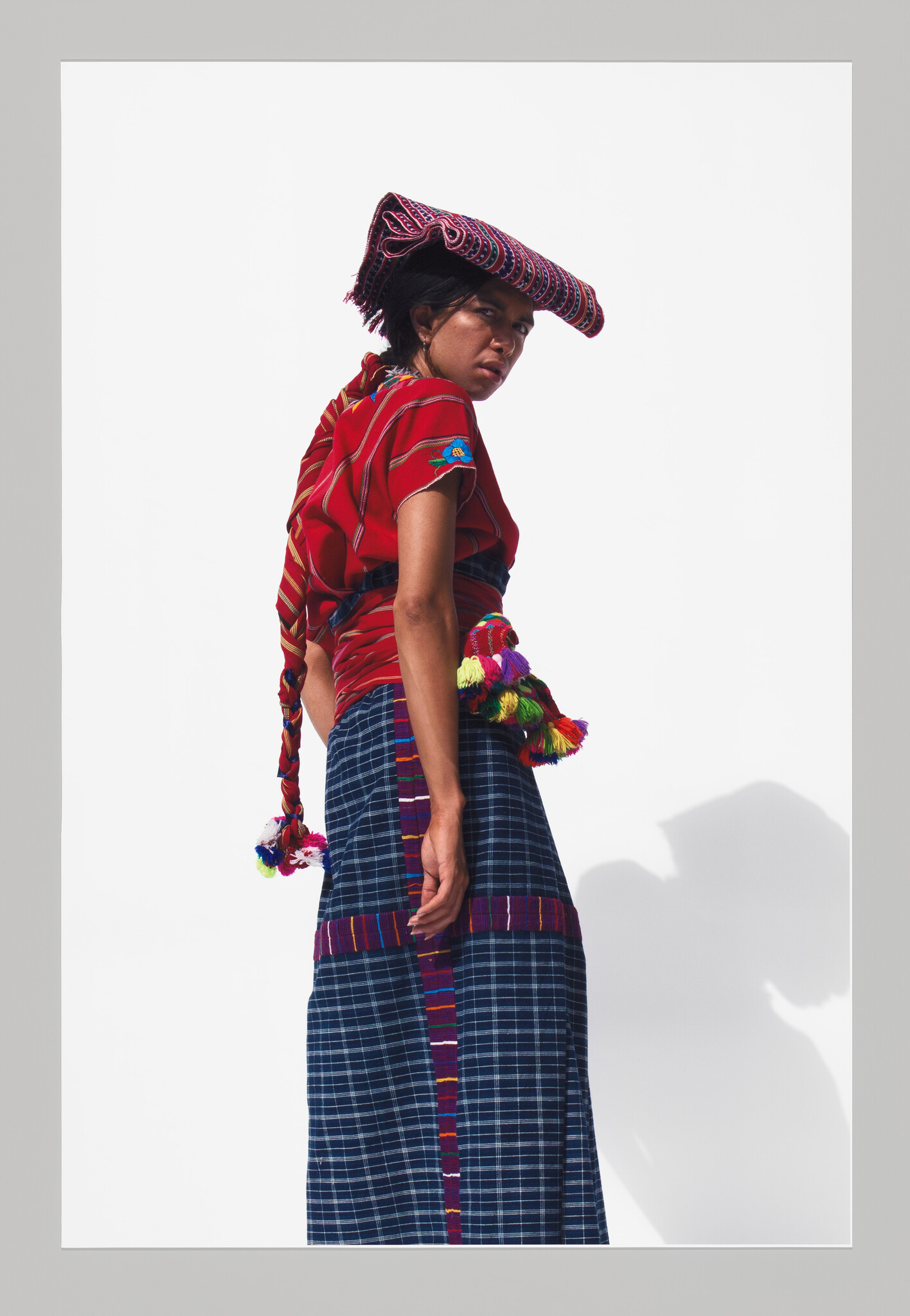 Young woman wearing traditional red blouse and patterned skirt looks over her shoulder with cloth on head.