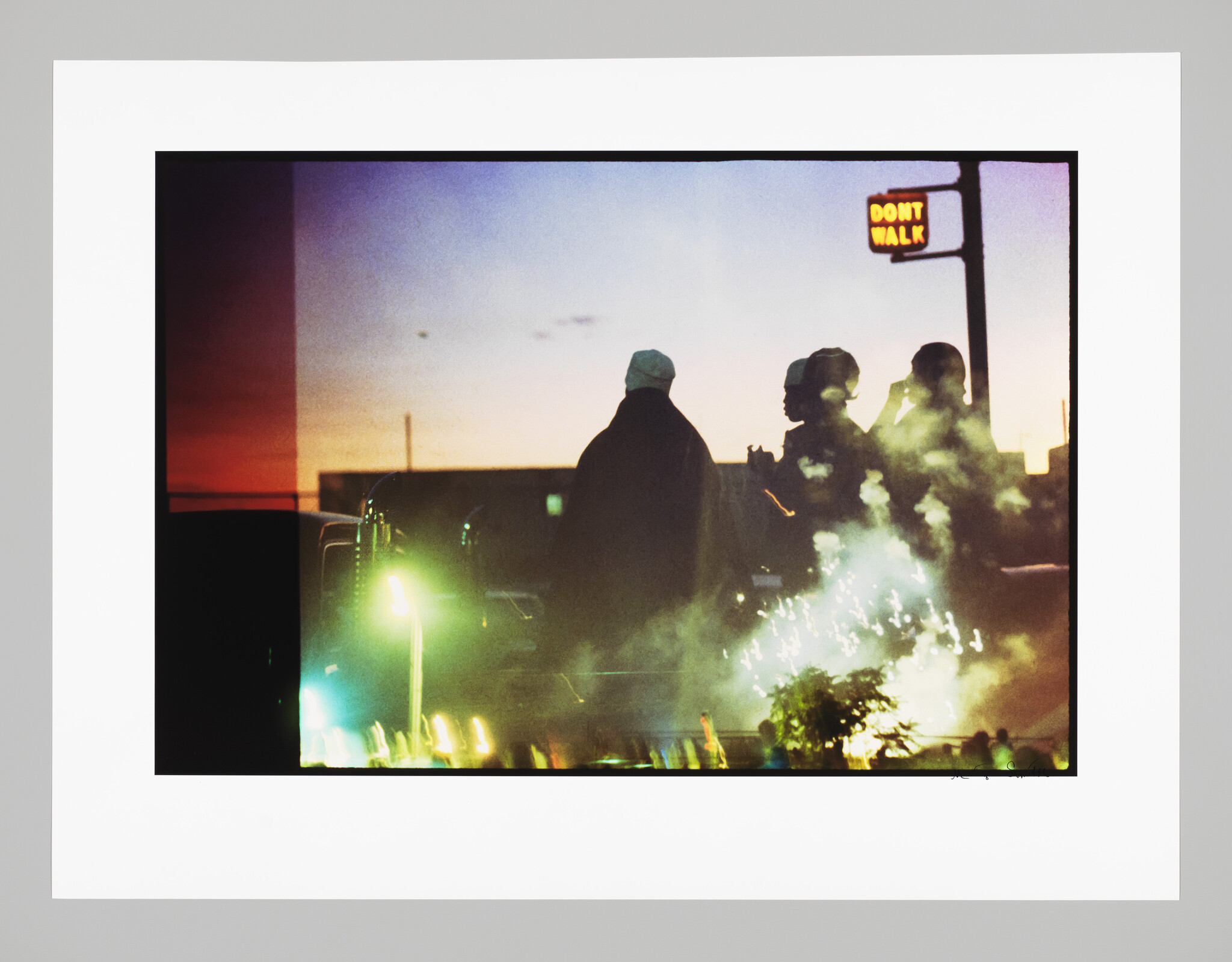 Three silhouetted people stand amid smoke and sparks under a lit Don't walk sign at dusk.