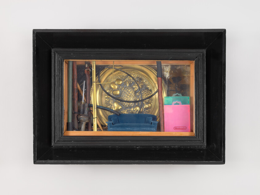 Framed shadow box containing a brass decorative plate, coiled wire, miniature blue sofa, and assorted objects.
