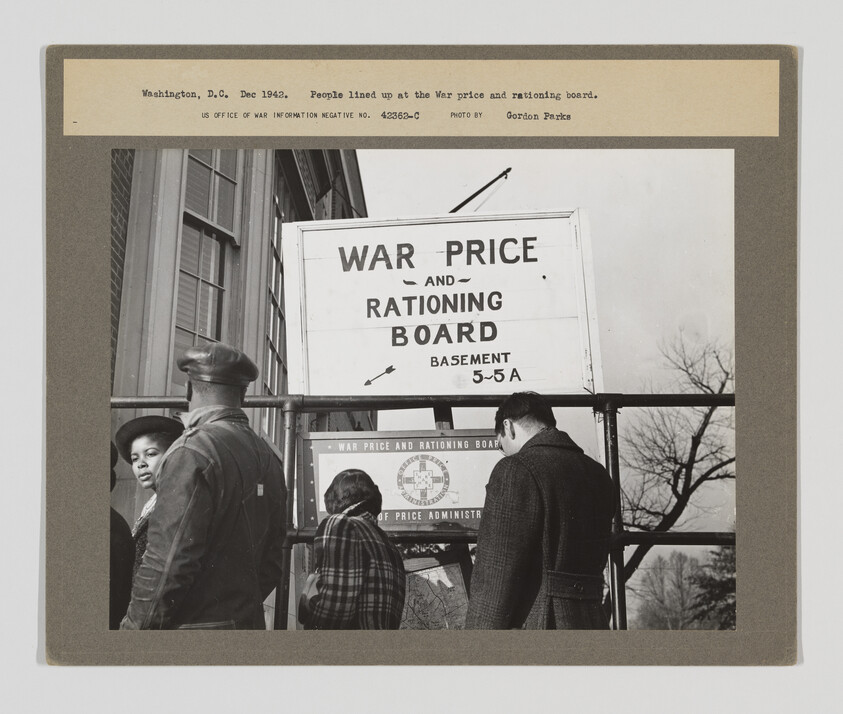 People wait in line outside the War price and rationing board office beneath a large sign.