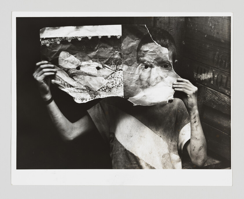 A person holds a torn photograph over their face, blending their eyes with the paper image.
