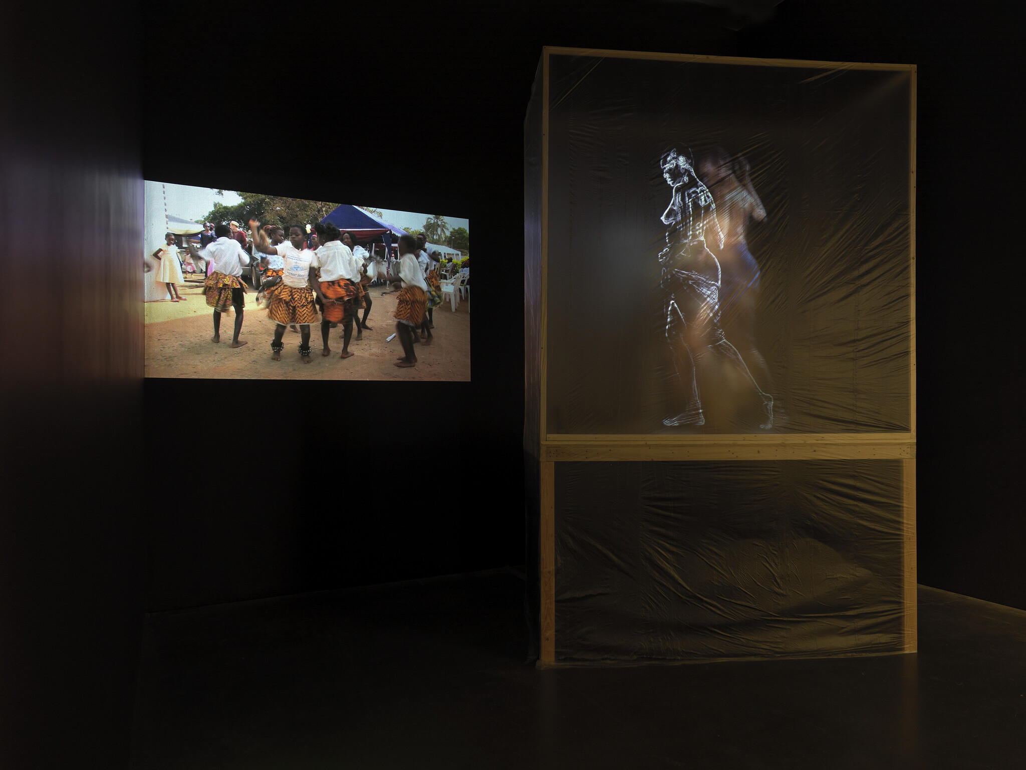 A group of people dance outdoors on a screen, next to a transparent box showing a projected figure.