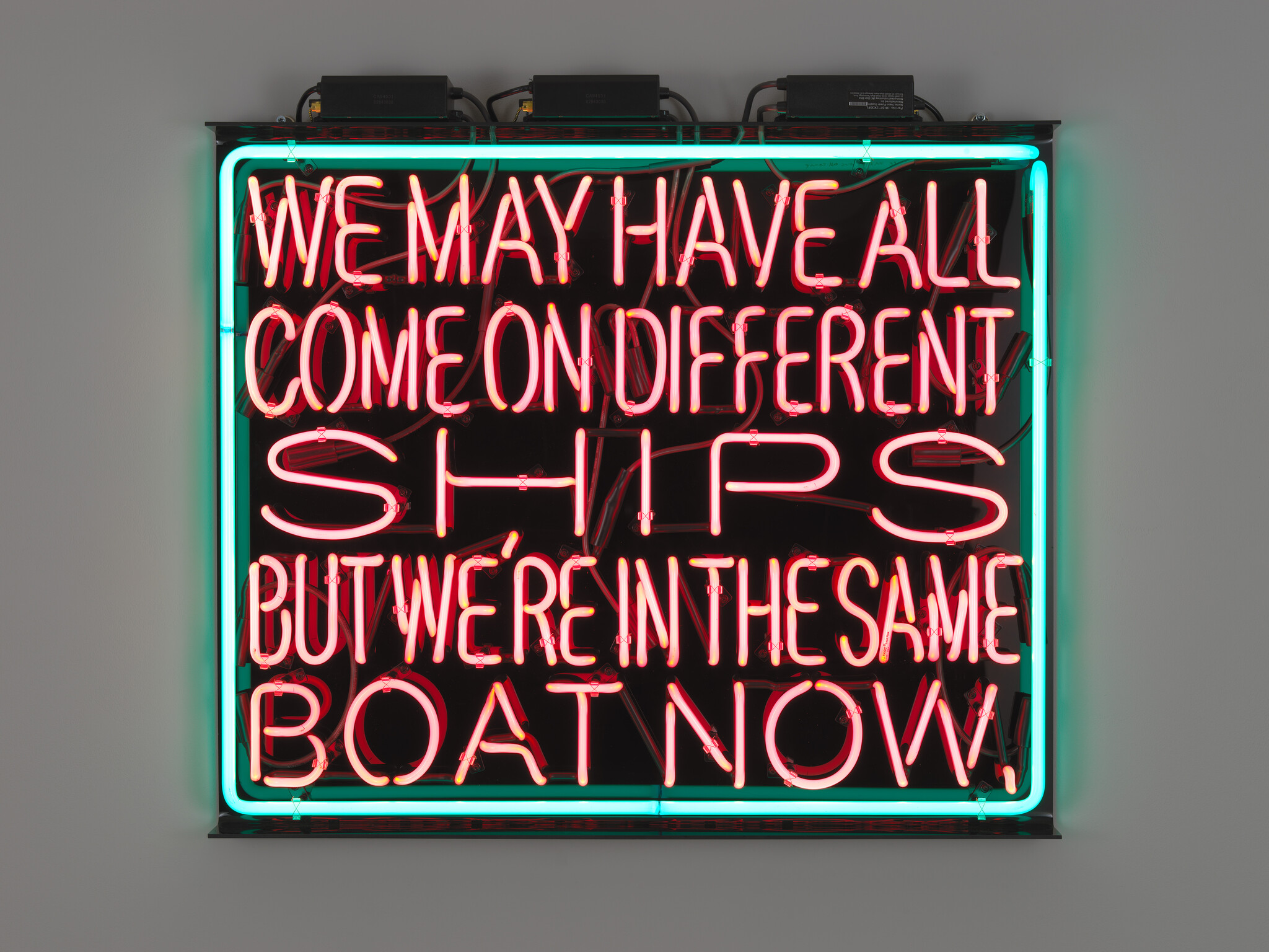A neon sign reads, "We may have all come on different ships but we're in the same boat now."