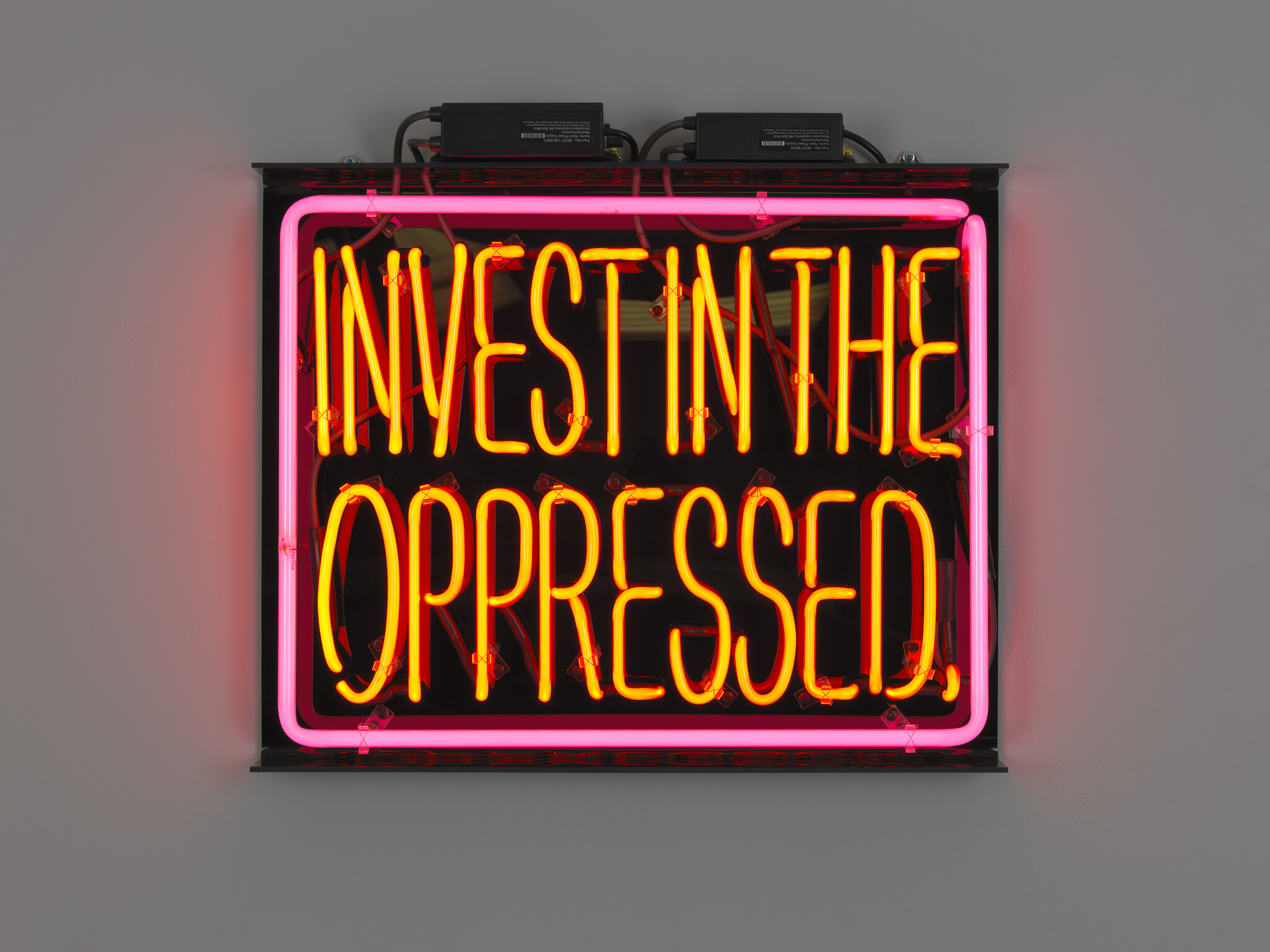 Neon sign reading invest in the oppressed in bright orange letters with a pink border.