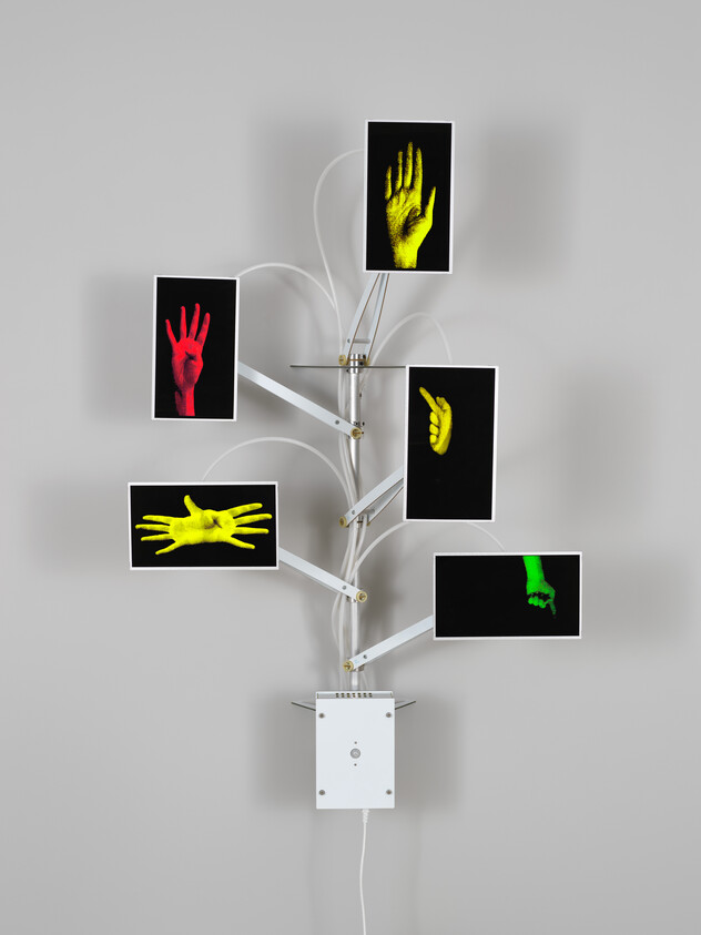 Wall-mounted electronic sculpture shows six colored hand images on branching screens like a tree.