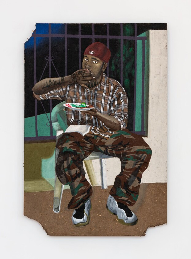 A man in a red cap and camo pants sits on a plastic chair eating food from a plate.