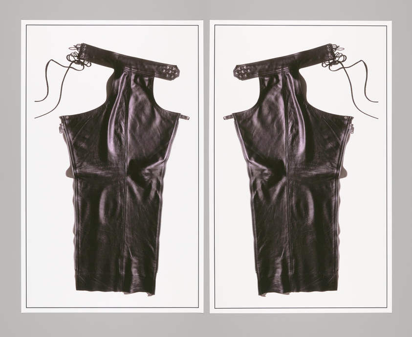 A symmetrical display of two black leather dresses with corset-like lacing at the top, hanging against a white background. Each dress features a zipper along the side and is presented without a mannequin, giving the appearance of floating in the frame.