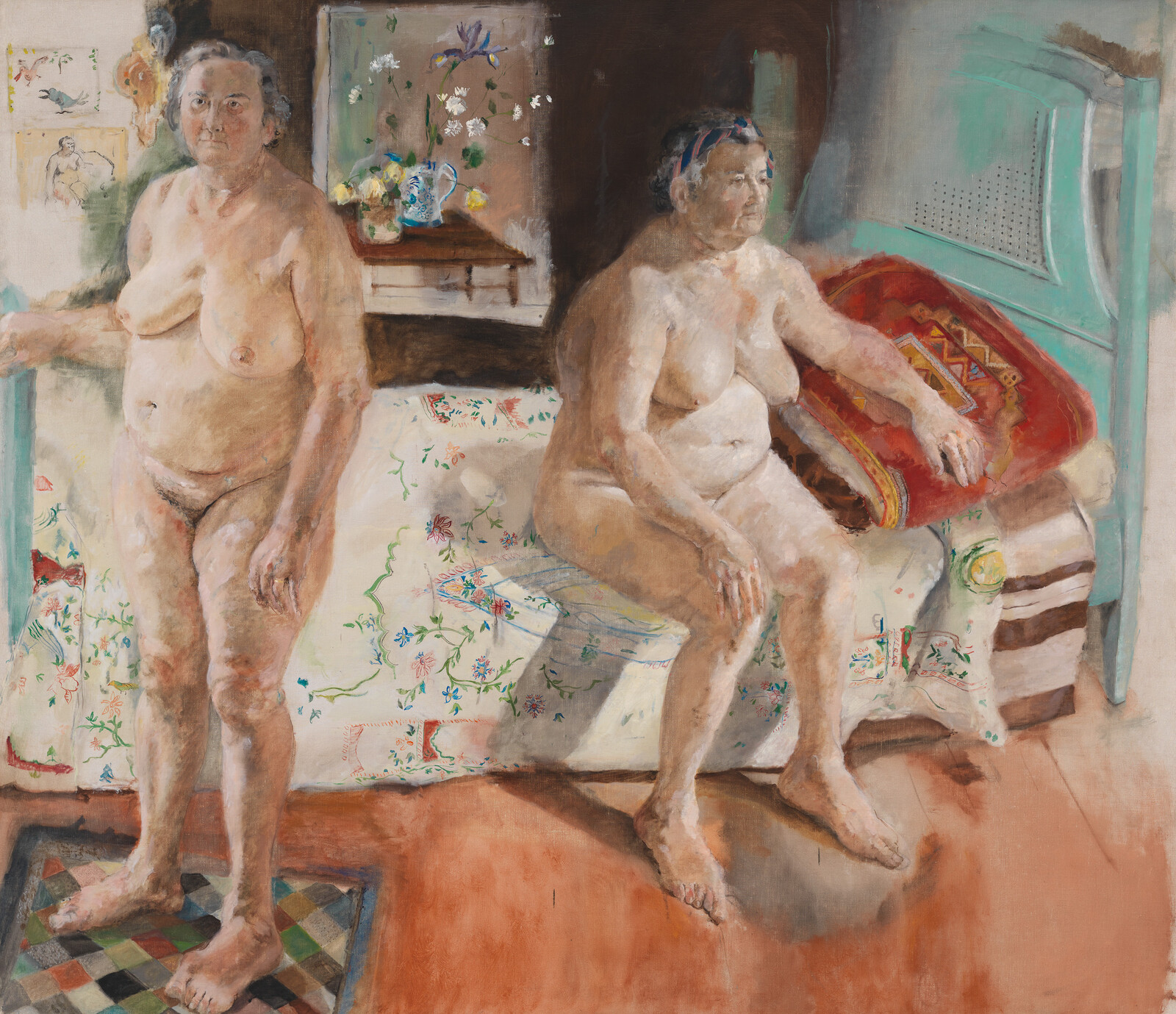 Two older nude women in a bedroom, one standing while the other sits on the bed.