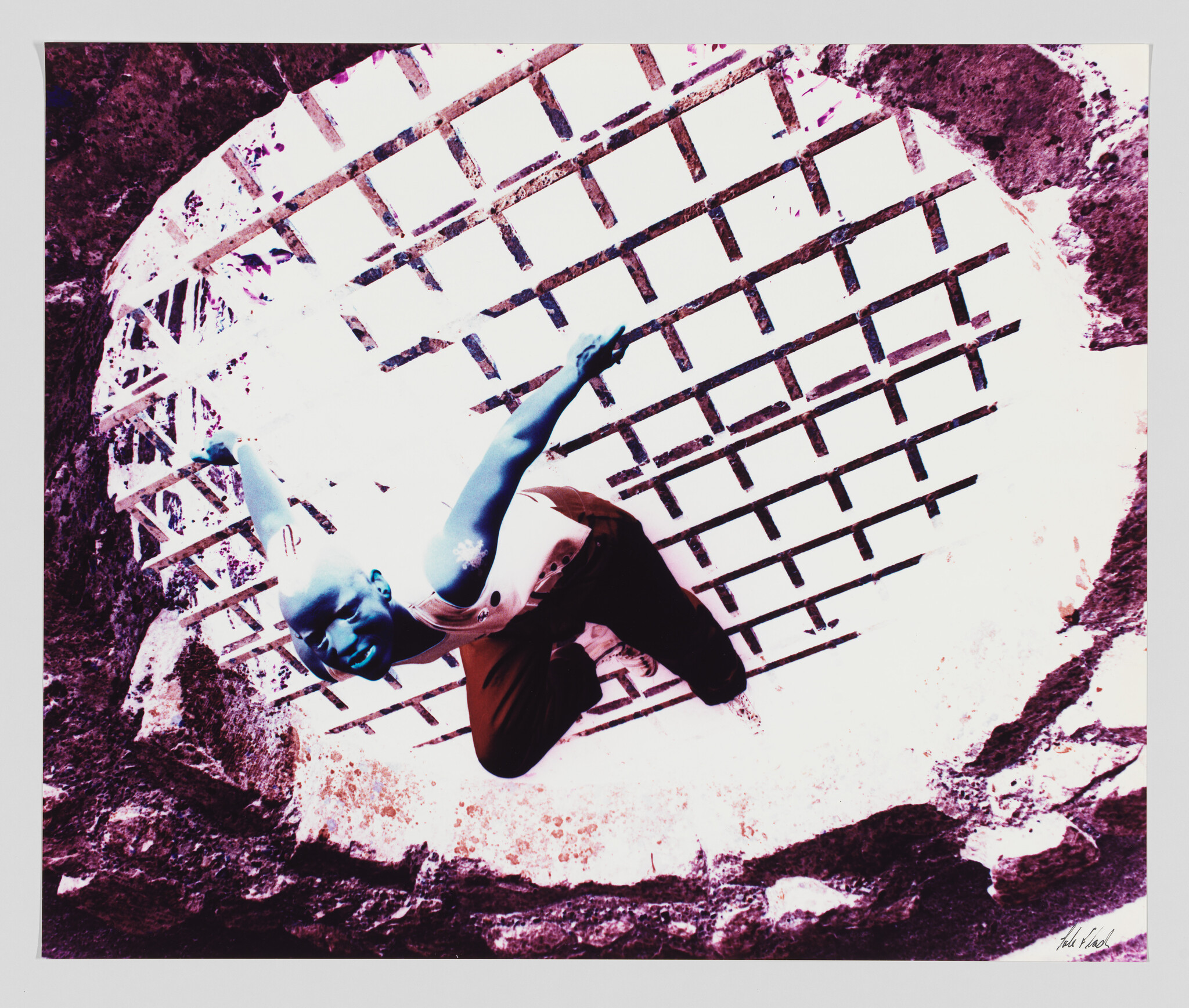A person leans over a circular barred grate with arms outstretched looking upward.