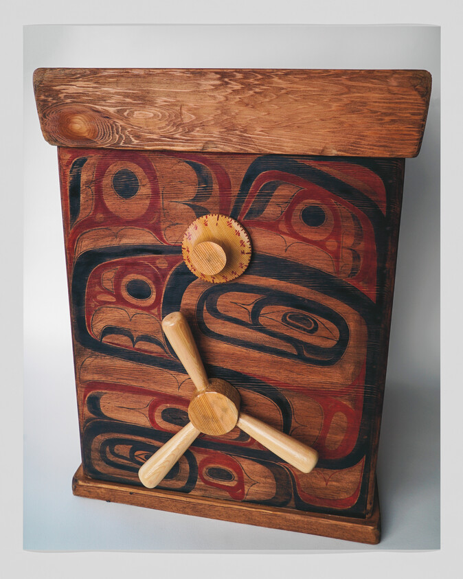 Wooden box with carved Indigenous-style painted designs and three-pronged wooden handle on front.