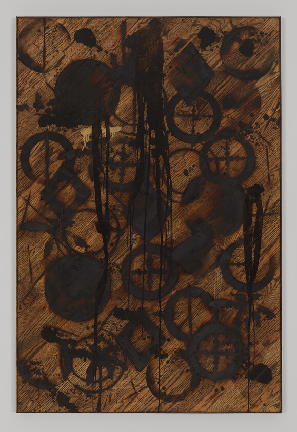 Abstract wooden panel with black circular stencils, drips, and splatters creating a layered pattern.