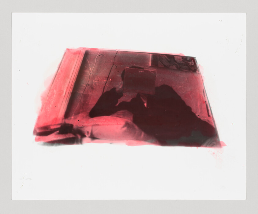 Person's dark silhouette reflected on a red-tinted window while holding a phone.