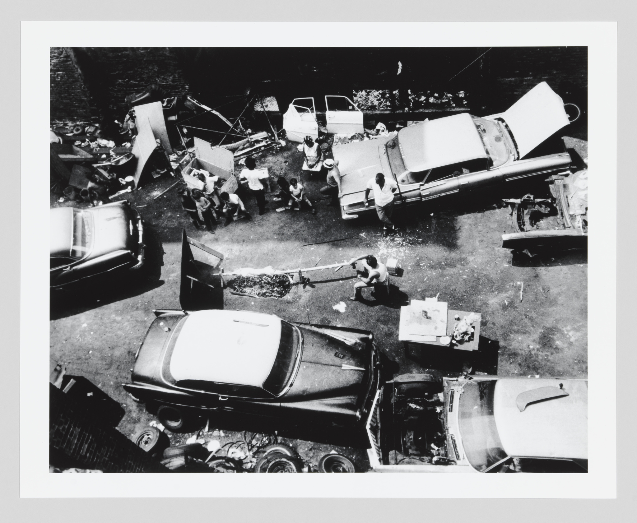 Overhead view of a cluttered junkyard with people and disassembled cars.