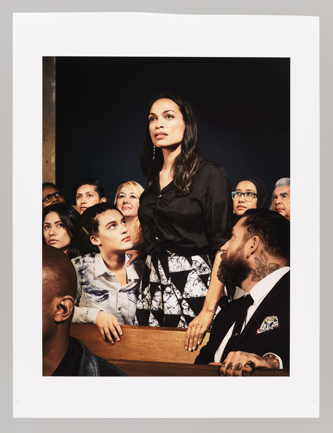 A diverse group of people looking attentively in the same direction, with a woman in the foreground standing out as she gazes upward with a thoughtful expression. The image captures a range of ethnicities and ages, suggesting a gathering of individuals with a common focus or interest.