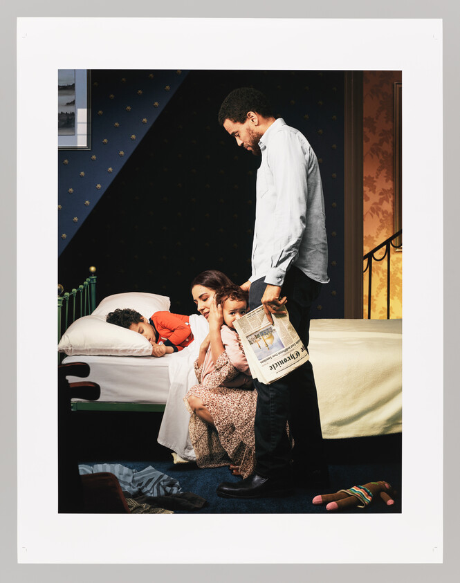A father holds a newspaper while a mother cuddles their child as another child sleeps.